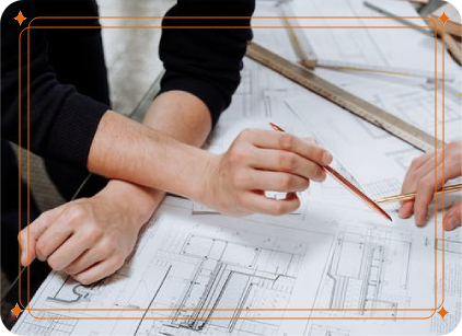 A person wearing a black sweater holding a pencil looks over blueprints