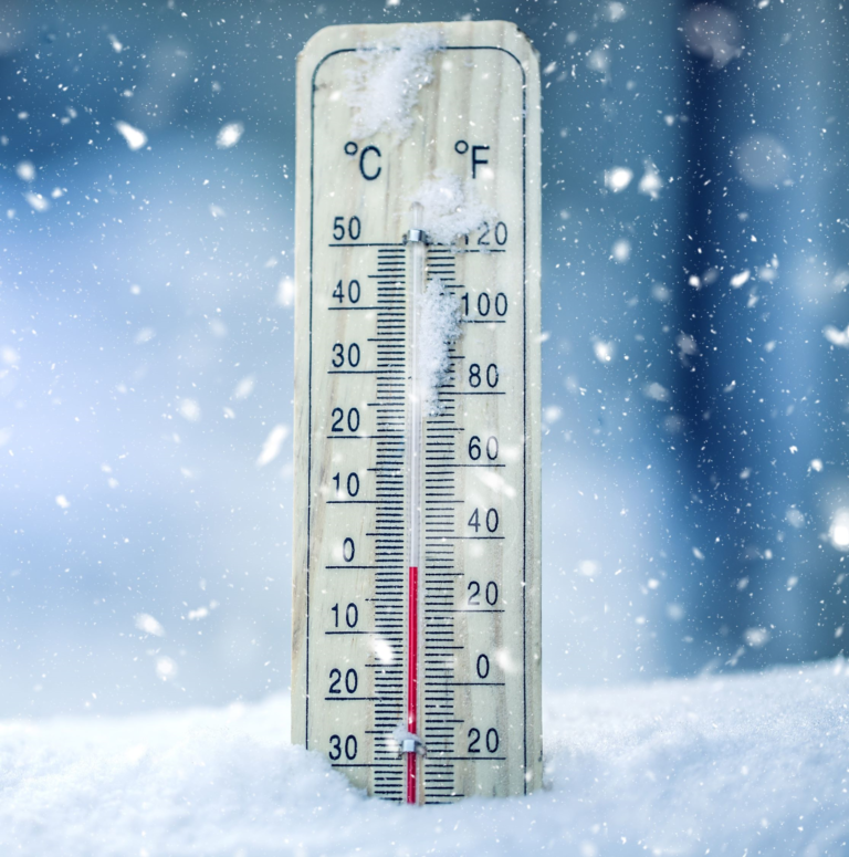 Thermometer showing zero degrees celsius resting in the snow with snow falling; frozen water pipes
